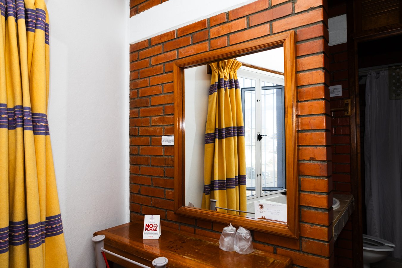 Espejo sobre muro de ladrillo y entrada al baño